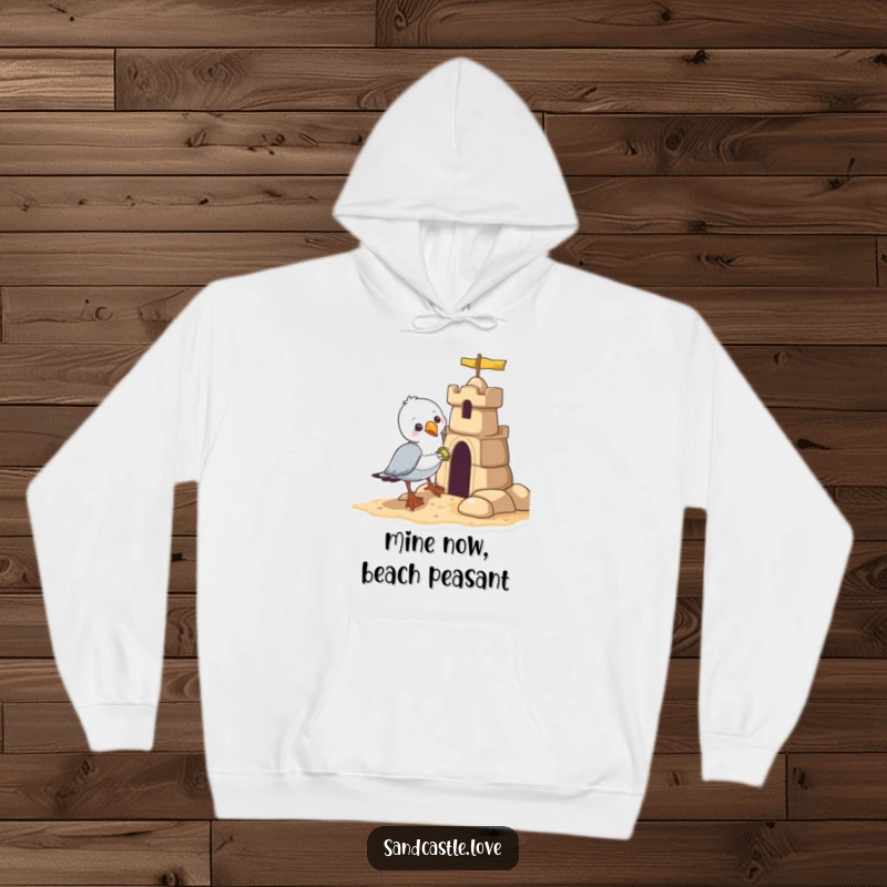 Funny seagull hoodie, a bandit seagull attempting to steal a shiny object from a sandcastle, humorous apparel.
