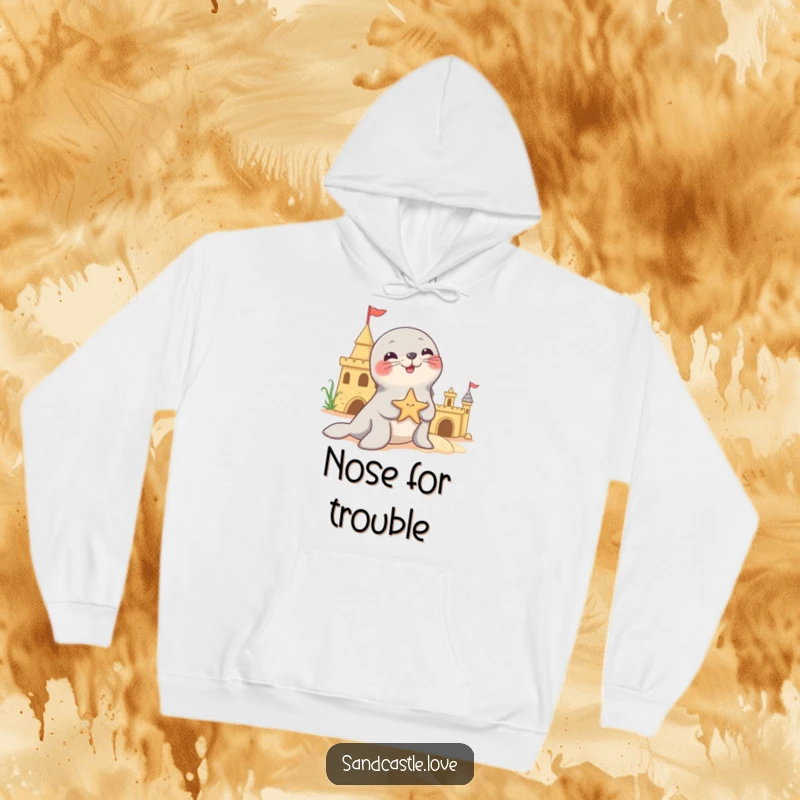 Funny hoodie depicting a playful seal character adeptly balancing a starfish on its sensitive nose, positioned beside a sandcastle structure.